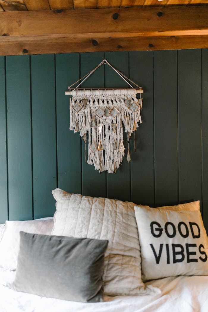 Cozy bedroom featuring a stylish macramé wall hanging and a pillow with 'Good Vibes' text.